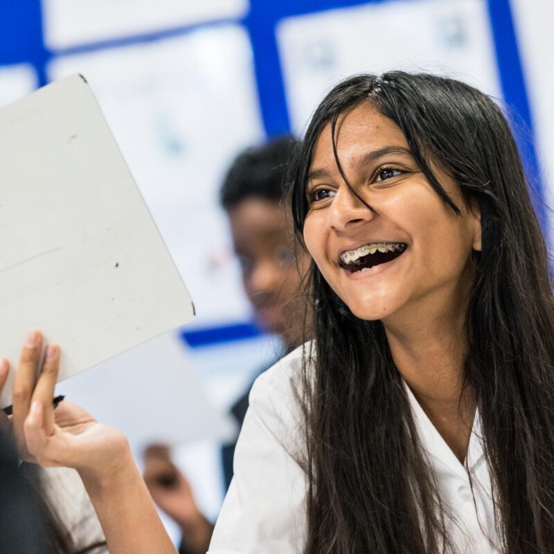 A girls with braces smiling and holding up a whiteboard